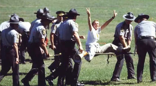 Ingrid Newkirk making peace signs being carried away by police officers