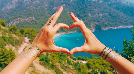 person holding up hands in the shape of a heart with a nature landscape background