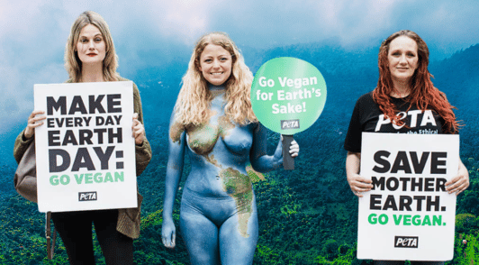 woman bodypainted like the earth with activists holding signs to go vegan for the planet
