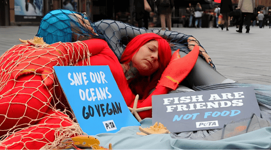 person dressed up as lobster with signs reading fish are friends not food and save our oceans go vegan