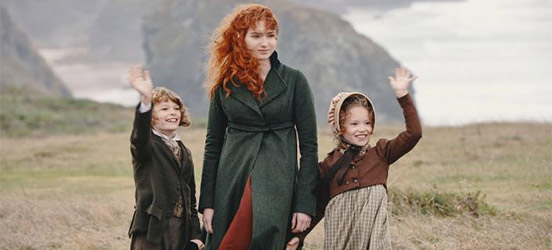 Poldark's Demelza stands on the coast with two waving children.