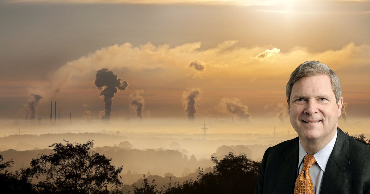 Tom Vilsack against a landscape of air pollution and smoke stacks