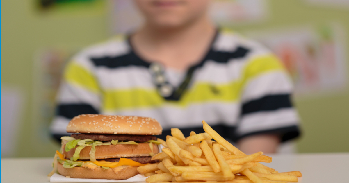young boy in front of a plate of fries and a burger