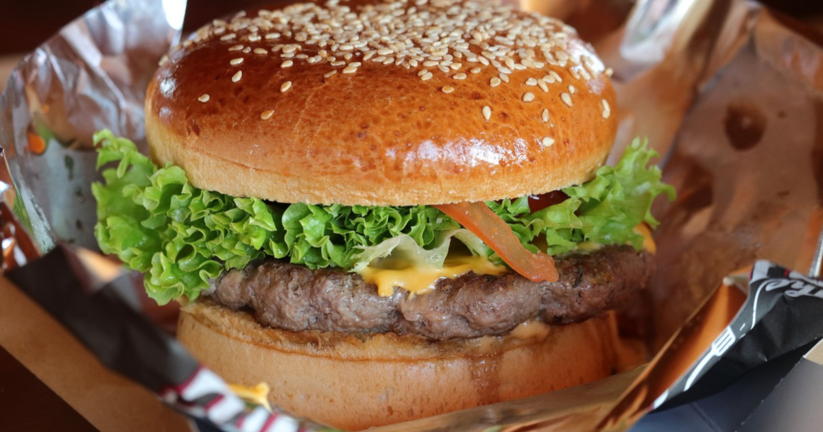 cheeseburger with lettuce tomato and onion on a sheet of aluminum foil