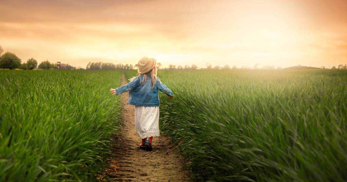child walking through a field at sunset