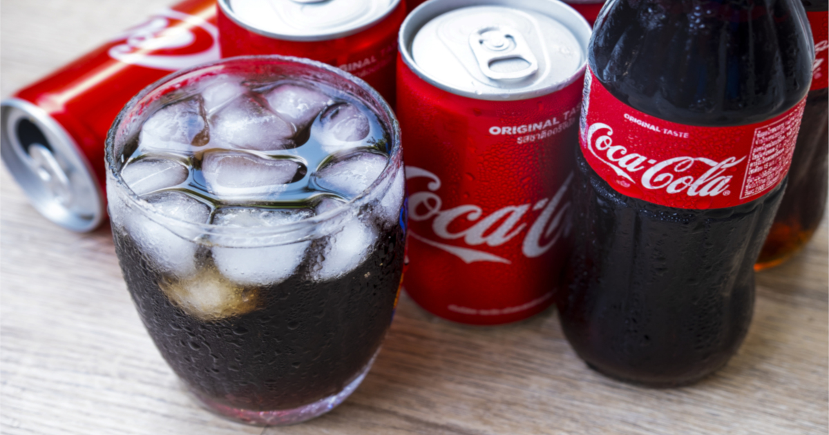 Coca Cola soda pop in a glass with ice cubes and in cans and a bottle