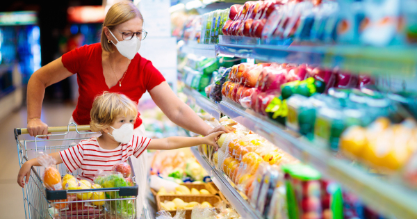 mother and son grocery shopping in the produce aisle of a supermarket while wearing cloth masks