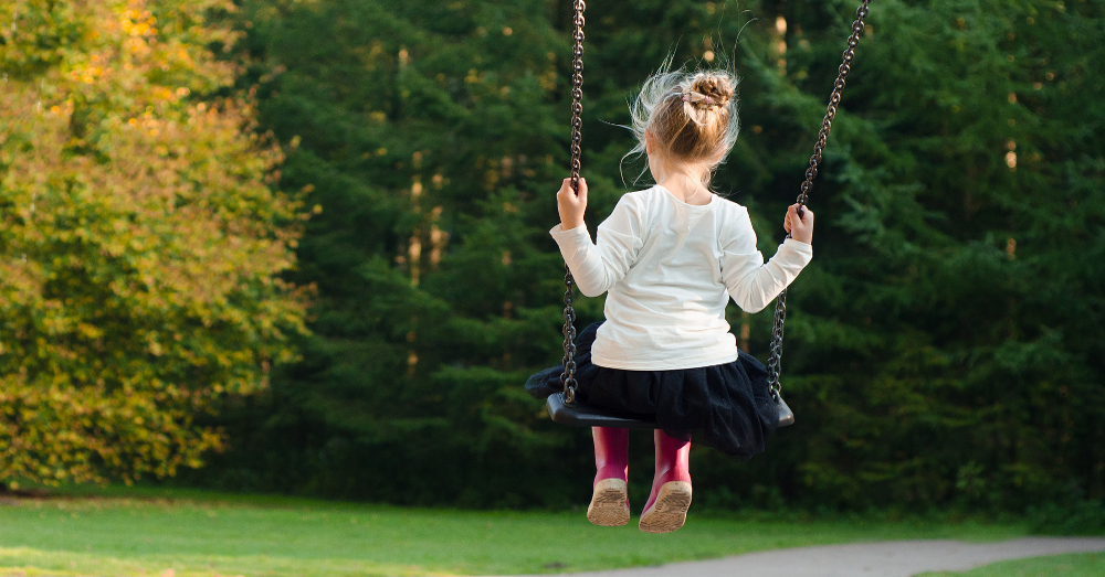 young girl playing on a playground swing set