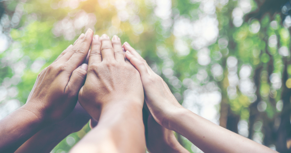 several people outdoors holding their hands together high in teamwork