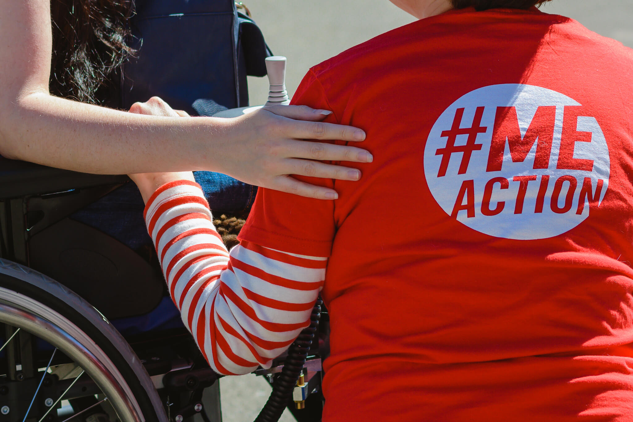 Person in #MEAction t-shirt kneels next to person in wheelchair