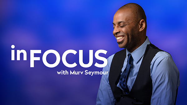 A man wearing a button-up shirt, tie and vest smiles while looking down. The words In Focus With Murv Seymour are placed alongside him.