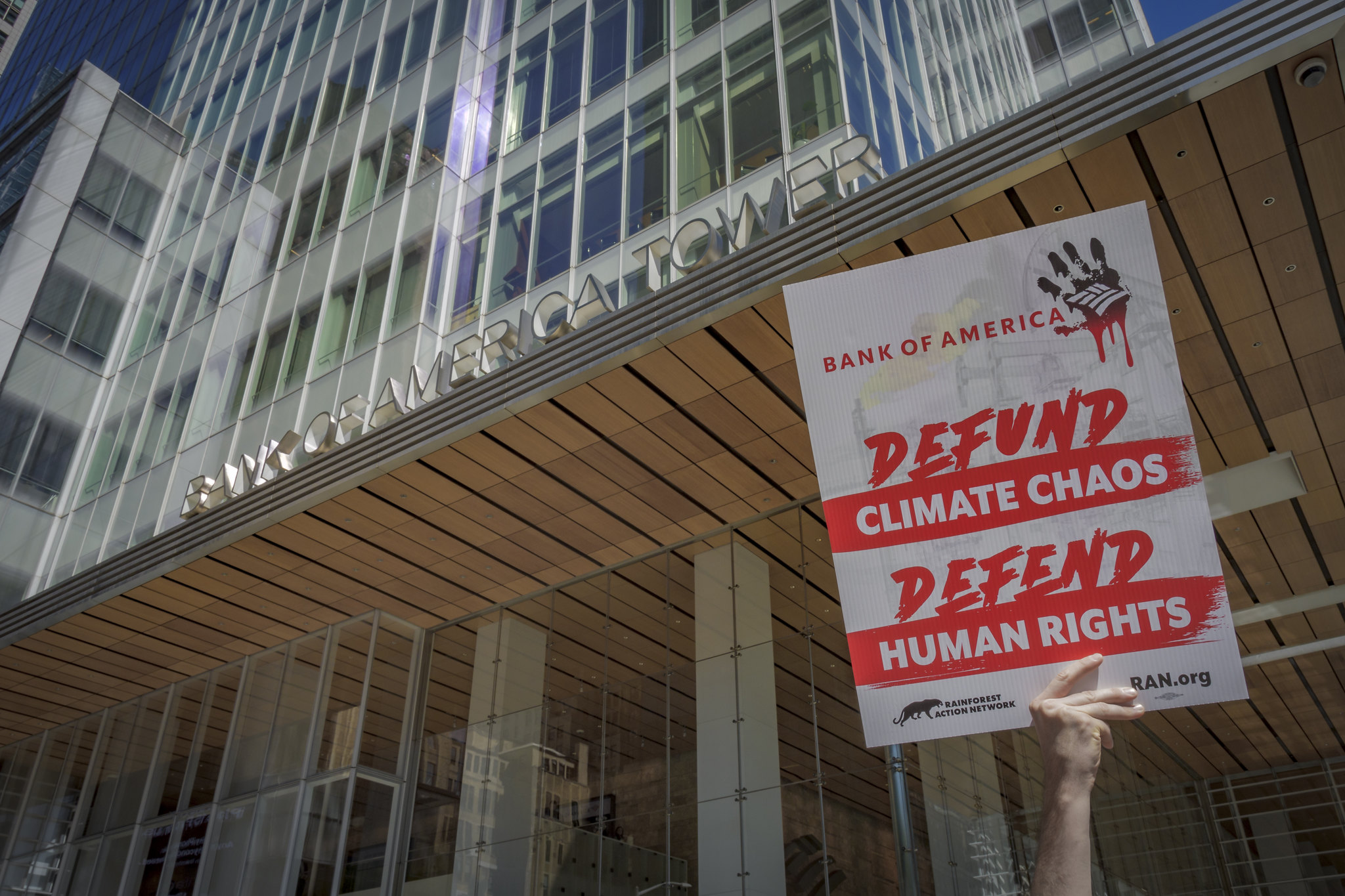 a protest sign held in front of camera that read defund climate chaos defend human rights
