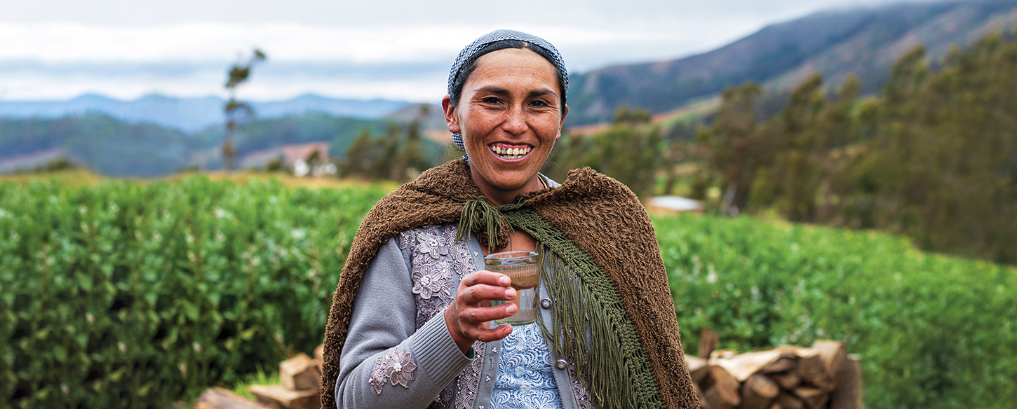 A woman in front of a field smiling and holding a glass of clean water