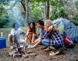 Friends gathered around a campfire outdoors, with smoke rising from the fire, illustrating exposure to wood smoke.