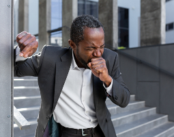 Man experiencing a cough outdoors, representing symptoms that can be associated with pneumonia.