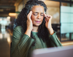 Woman pressing her temples while sitting at a computer, appearing to have a headache.