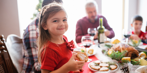 Child enjoying a cookie at a festive family dinner with assorted foods.