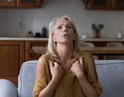 A woman on a couch touches her throat and looks uncomfortable, suggesting breathing issues related to menopause.