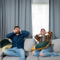 A couple sitting on the couch covering their ears