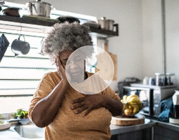 Woman in a kitchen holding her chest, illustrating symptoms related to sarcoidosis.