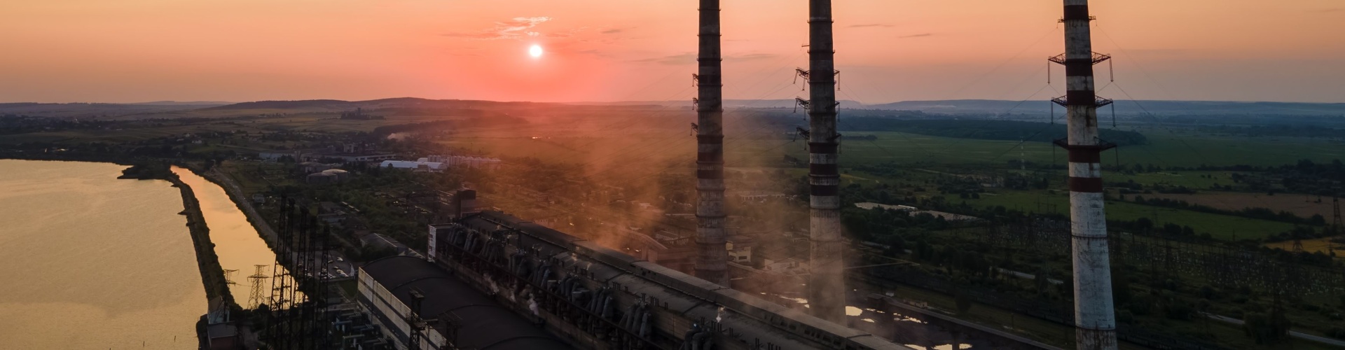 Aerial view of coal power plant high pipes with black smoke moving upwards polluting atmosphere at sunset