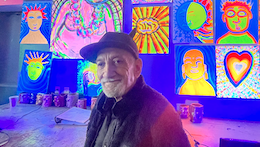 Ken Segal is seen in front of a wall of fluorescent art