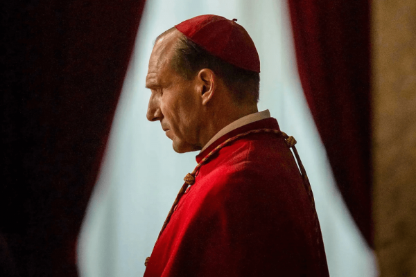 still from film: elderly white man wears red Catholic vestements