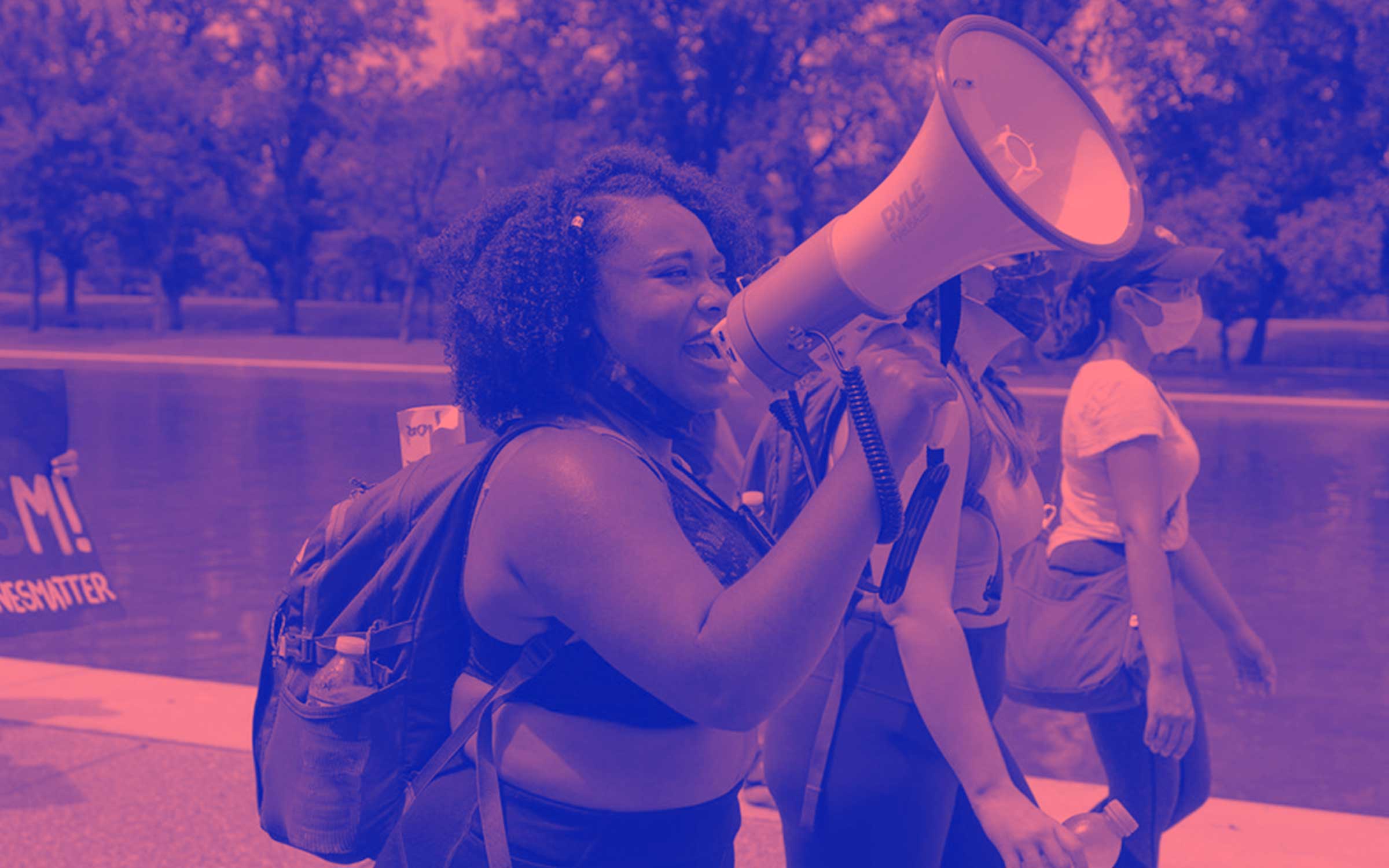 a young Black woman marching and protesting while talking into a megaphone