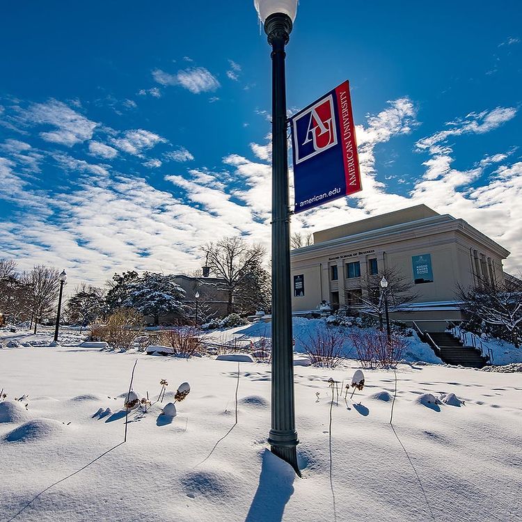 Snow-covered hill. Light pole with AU sign in front of Kogod School of Business.