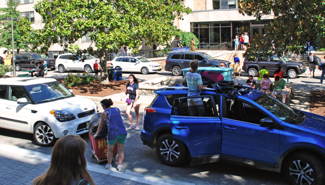 Cars in front of a residence hall with staff unloading them