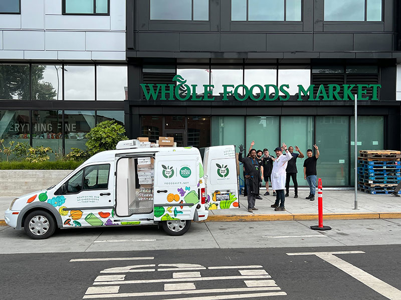 people waving near a van on a street in front of a store