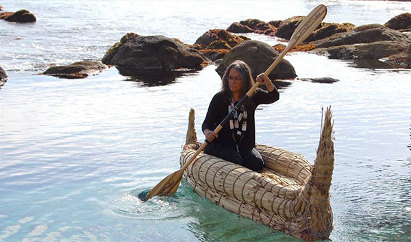 photo of a woman paddling a watercraft woven of reeds