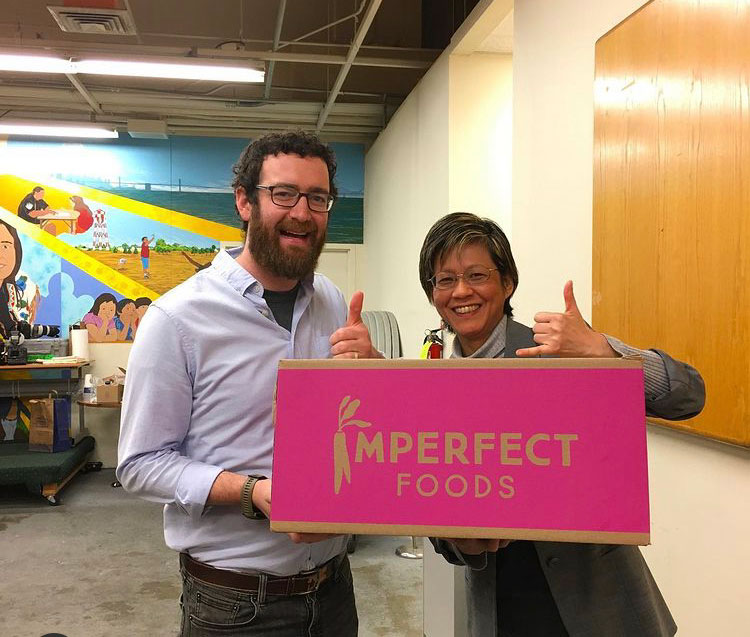 photo of people holding a box that has words, imperfect foods