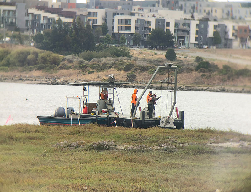 photo of a boat at a shoreline, people working a crane