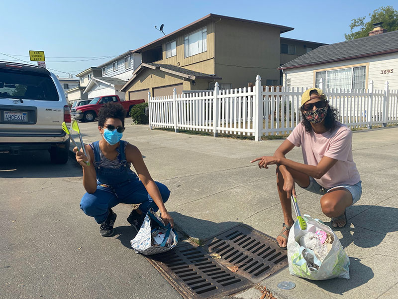 photo of masked people pulling trash from a storm drain with salad tongs