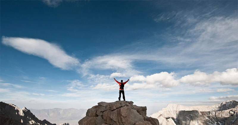 photo of a person on a high summit, arms wide in celebration
