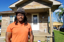 a Black man standing in front of a yellow house