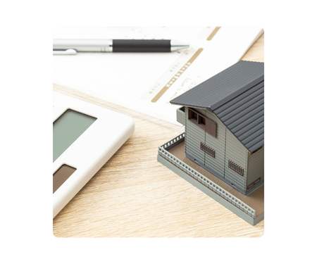 Miniature model house on a desk with a calculator and documents.