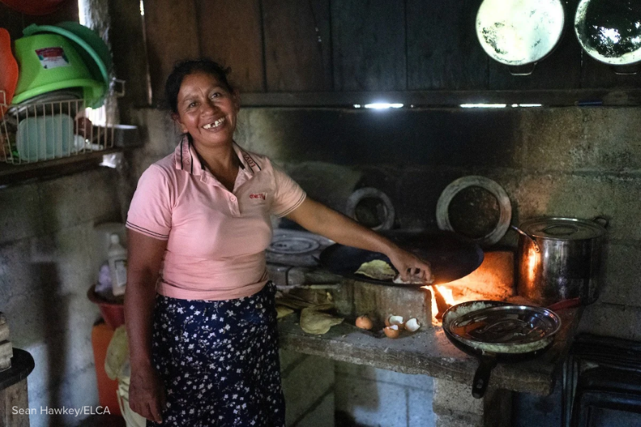 A woman smiling and cooking tortillas on a stove.