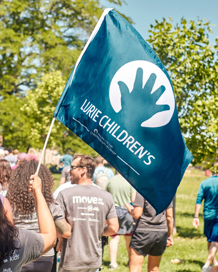 A photo of a woman participant waving the Lurie Children's flag.