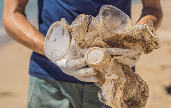 Close-up of trash picked up  on the beach by someone wearing white gloves - sand is seen in the background