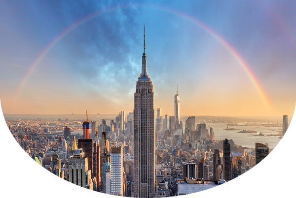 Photo of the Empire State Building in front of New York City with a rainbow on top of it
