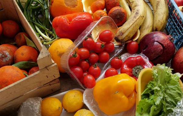 Group of fresh produce including tomatoes, lemons, bananas, lettuce, bell peppers, oranges, and more - some in wooden crates, some in plastic