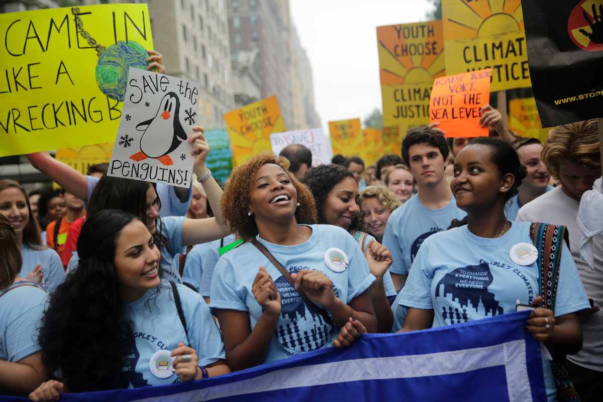 Three young women of color stand in a crowd of people holding signs and gathered in New York City to protest climate change