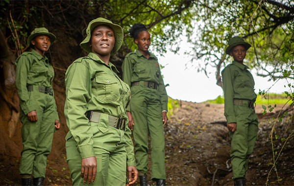 Four female rangers stand together in green uniforms under a tree.