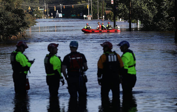 Responders stand in flooded streets with a lifeboat in the distance