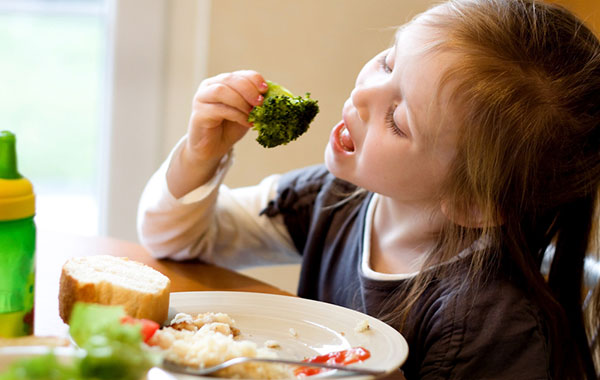 Child eating a broccoli snack at a dinner table