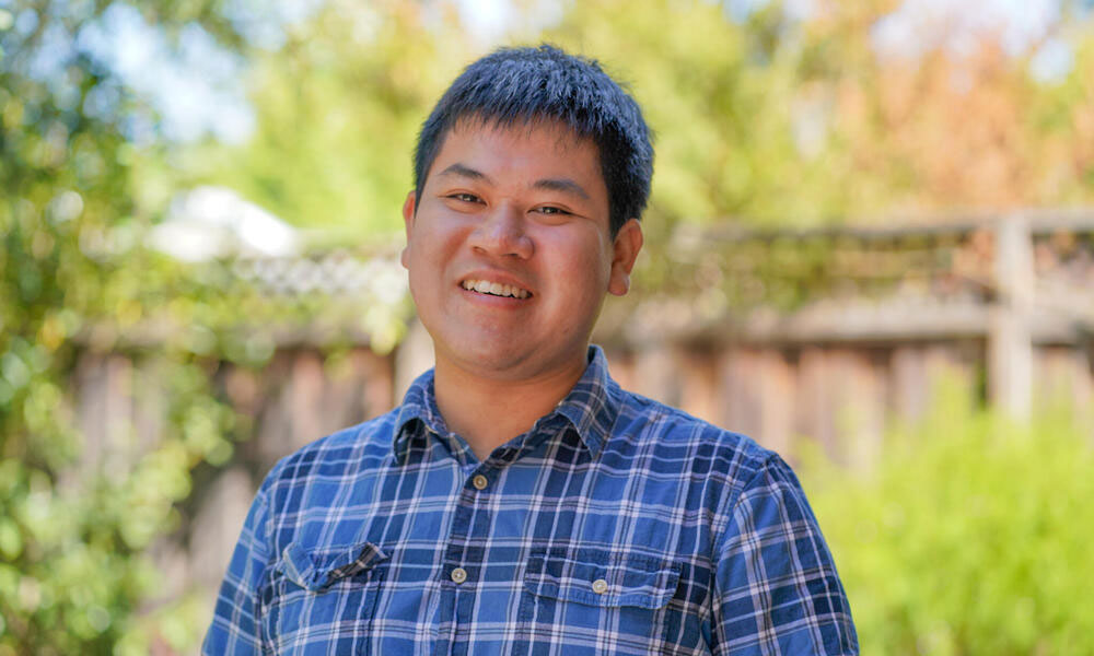 Portrait of Peter Pham in a blue flannel shirt standing outside