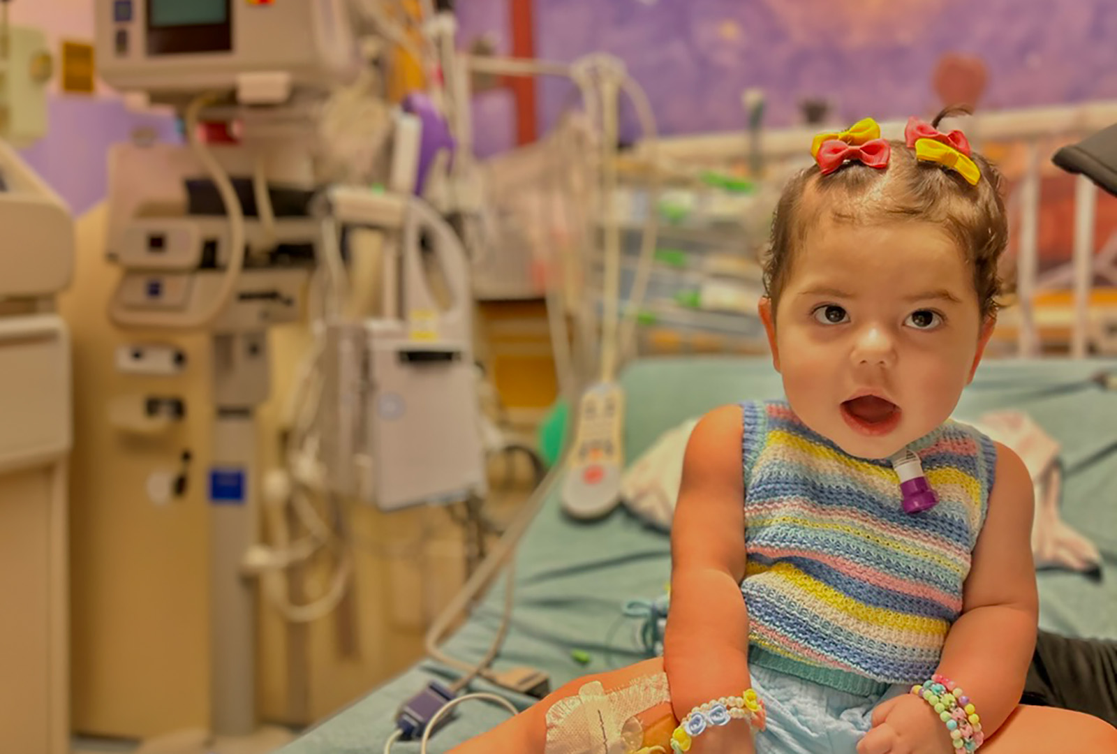 toddler girl wearing bows in her hair sitting on hospital bed