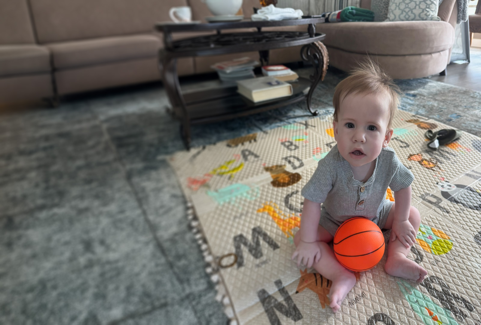Baby sitting on the floor in a home with a toy basketball in his lap.